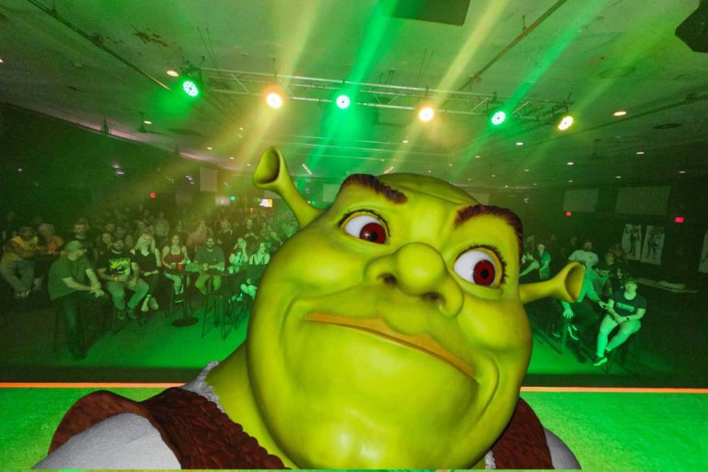 La imagen muestra la cara de Shrek sobre el decorado de un espectáculo burlesco con temática de Shrek.