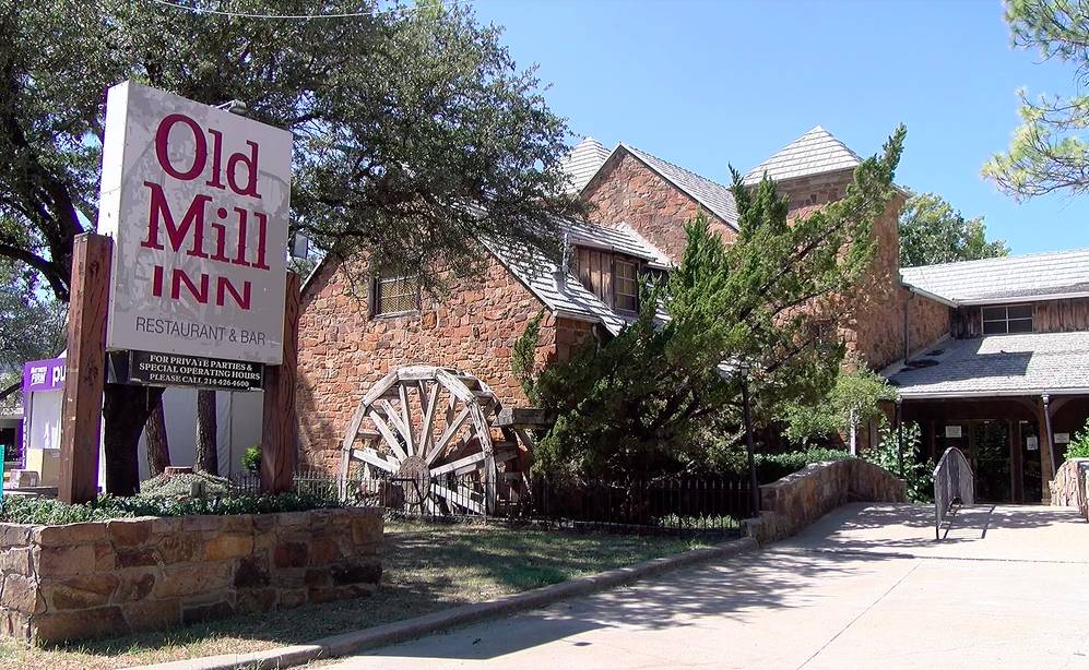 La imagen muestra el letrero y el exterior del Old Mill Inn, con su rueda de paletas. 