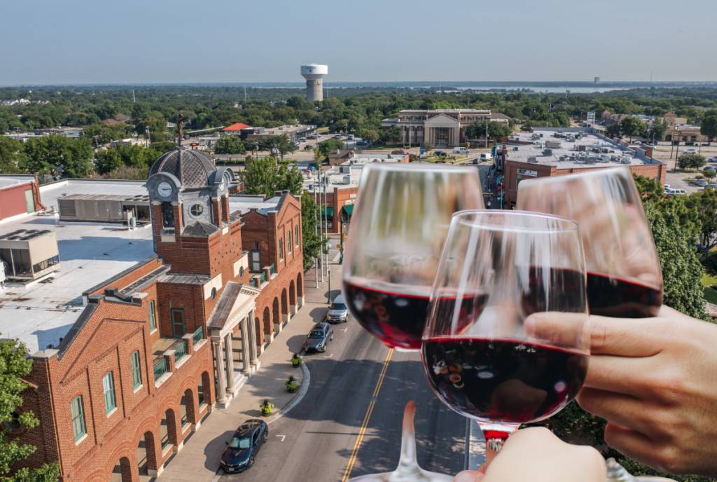 Image shows downtown Grapevine with an image of people raising wine glasses in the corner.