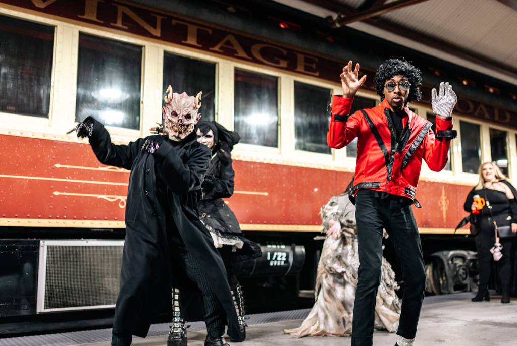Image shows two people in Halloween costumes posing in front of a train.