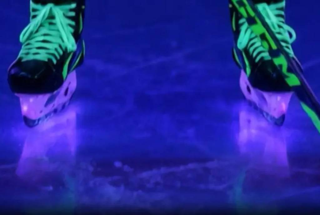 Image shows a hockey player's skate on a black-lit ice.
