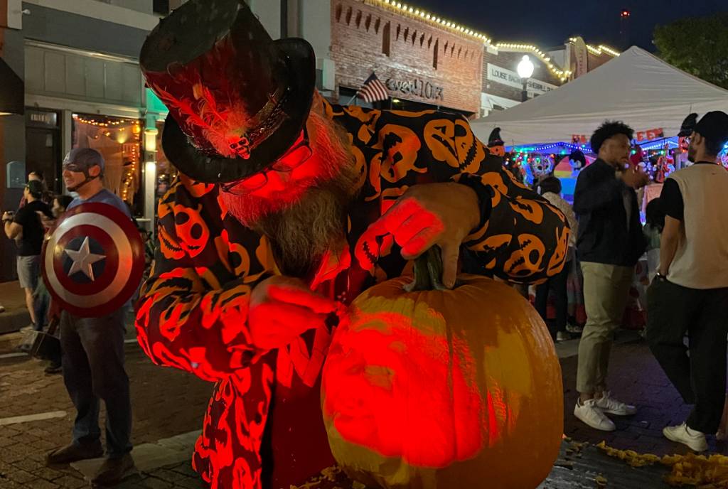 Image shows a man carving a jack-o-lantern at the Plano festival.