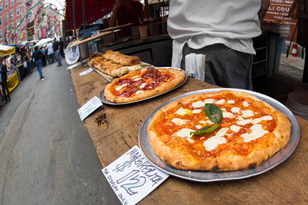 La imagen muestra a un vendedor de pizza en un festival italiano.