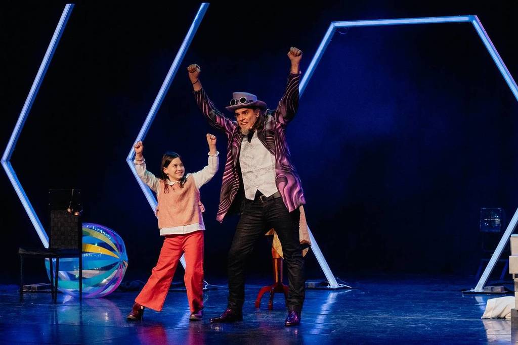 A magician wearing a top hat on stage with a kid