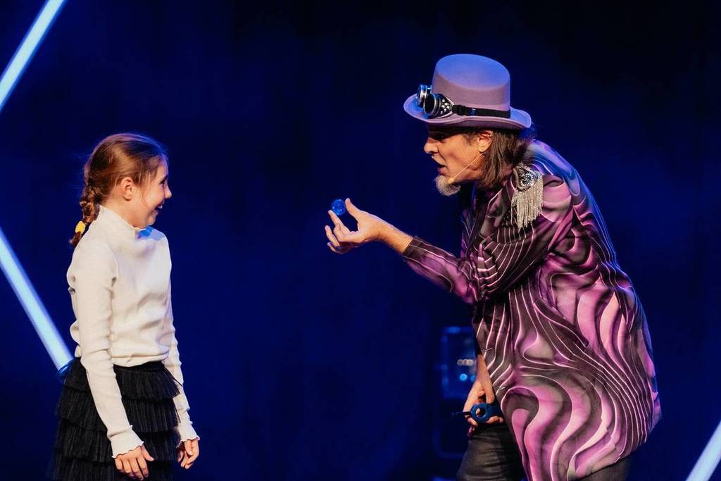 A magician performing a coin trick on stage in front of a young child