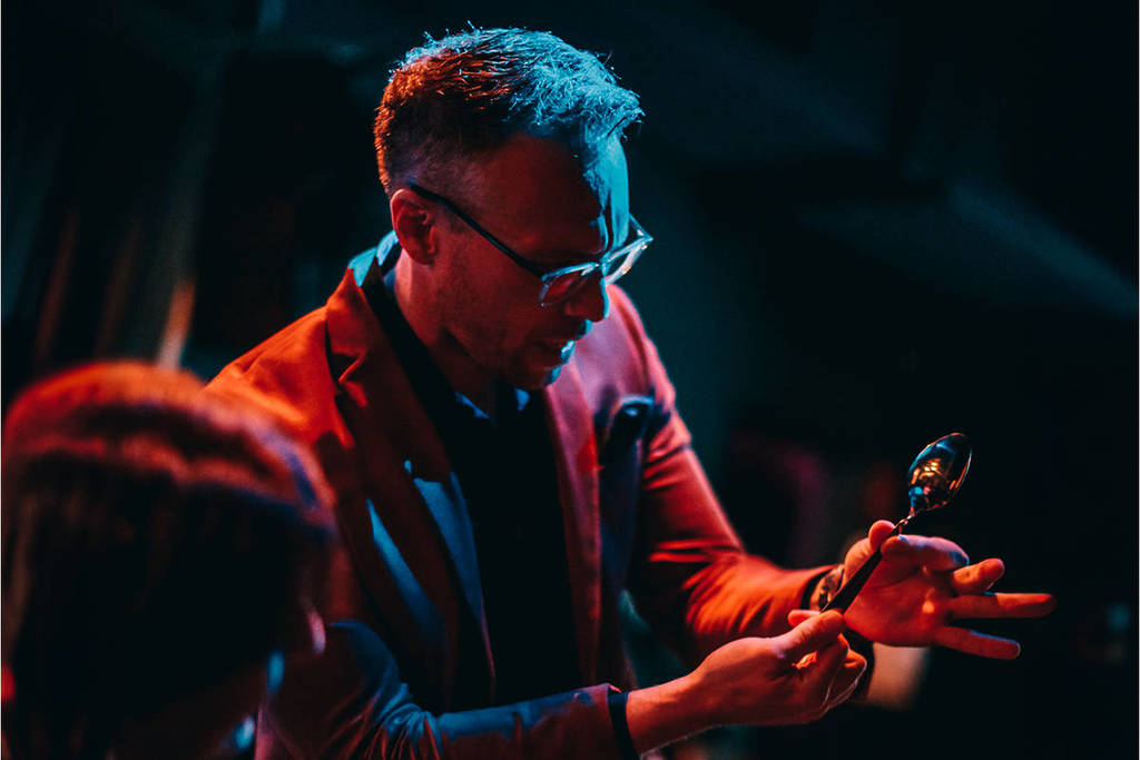 A magician holding a spoon on stage at a magic show