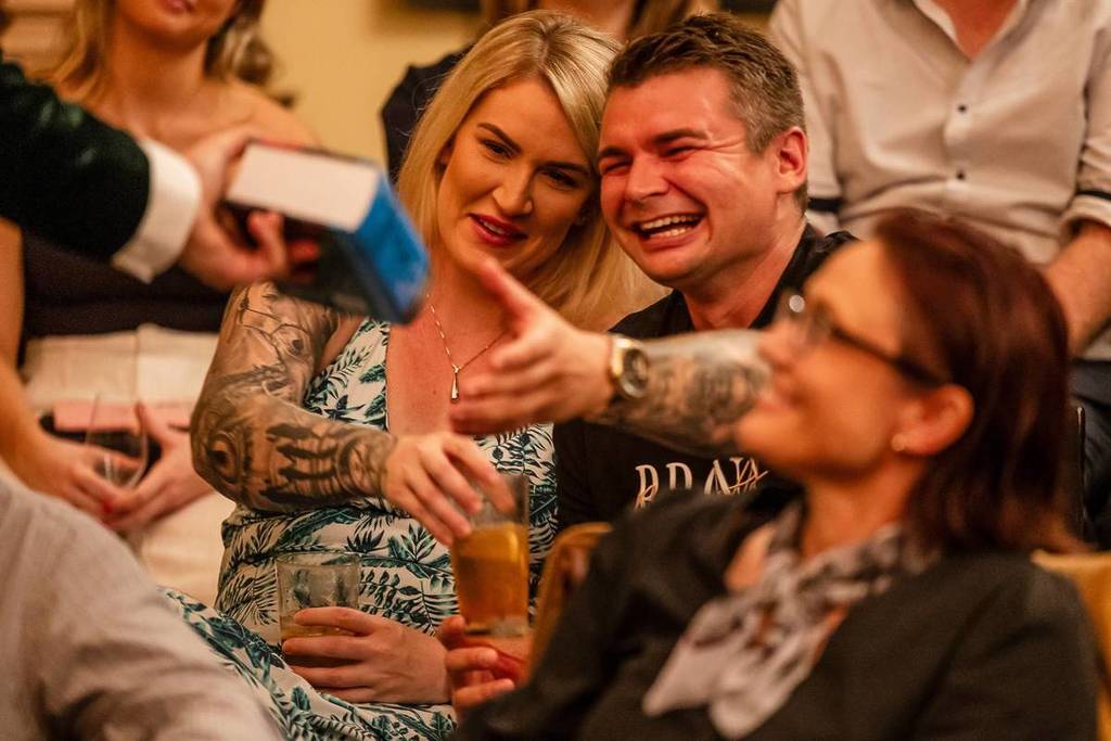 A couple laughing with cocktails in hand at a magic show