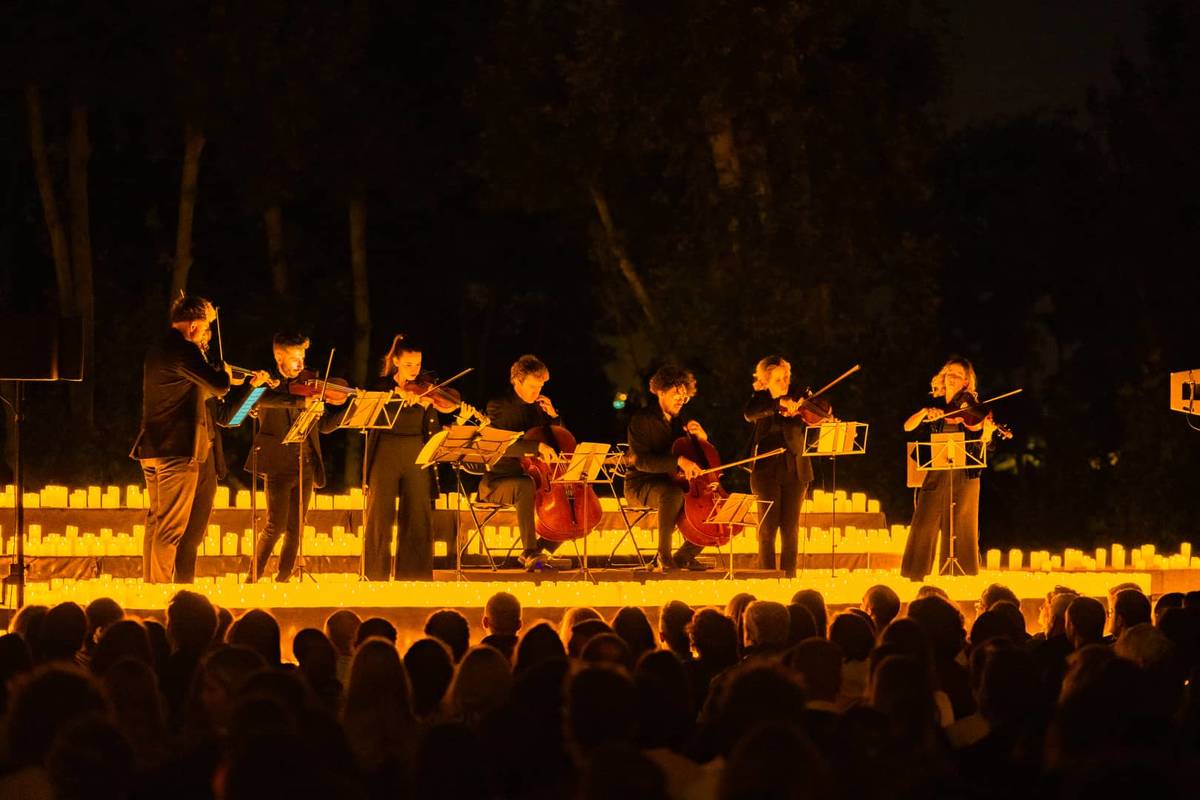 string quartet plays outside on a stage lit by hundreds of candles