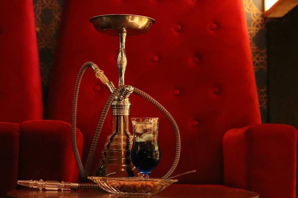 A shisha pipe on a table before a red velvet chair.