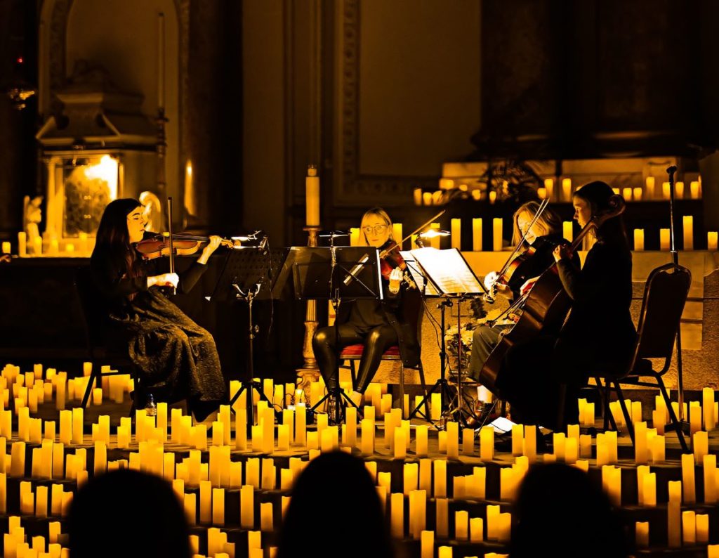 A string quartet performing a Candlelight concert on a stage surrounded by hundreds of flickering candles.
