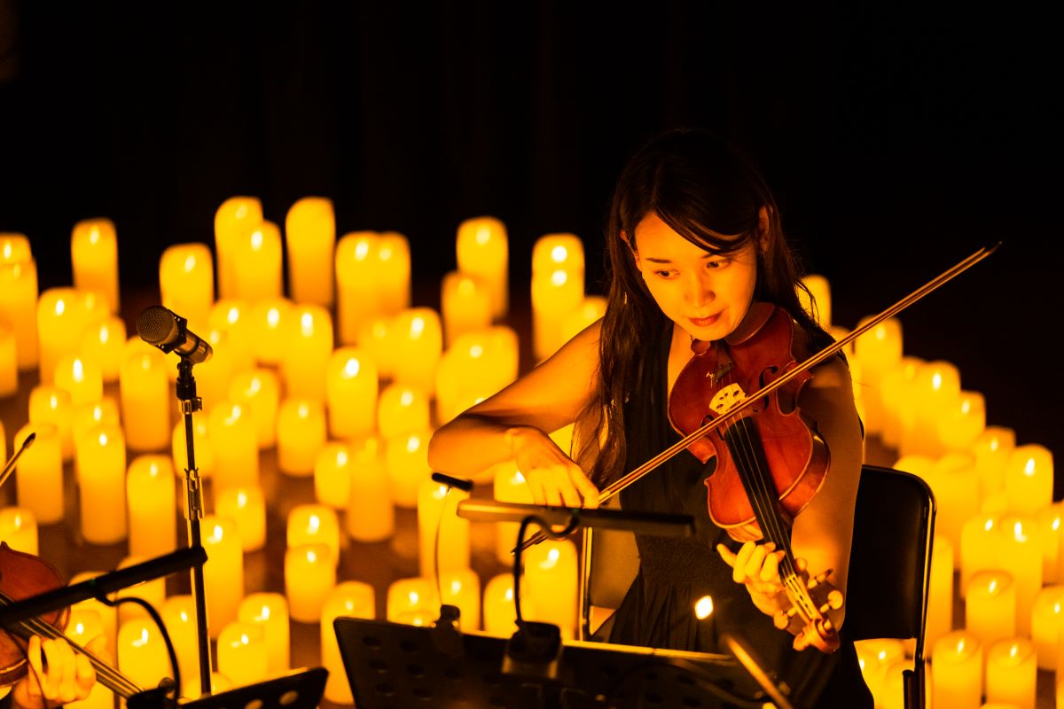 Musikerin spielt bei einem Candlelight-Konzert auf ihrer Geige, etliche leuchtende Kerzen im Hintergrund