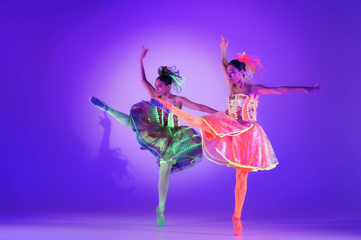 Zwei Ballerinas tanzen nebeneinander mit erhobenen Armen und Beinen bei Ballet of Lights: Cinderella in funkelnden Kostümen