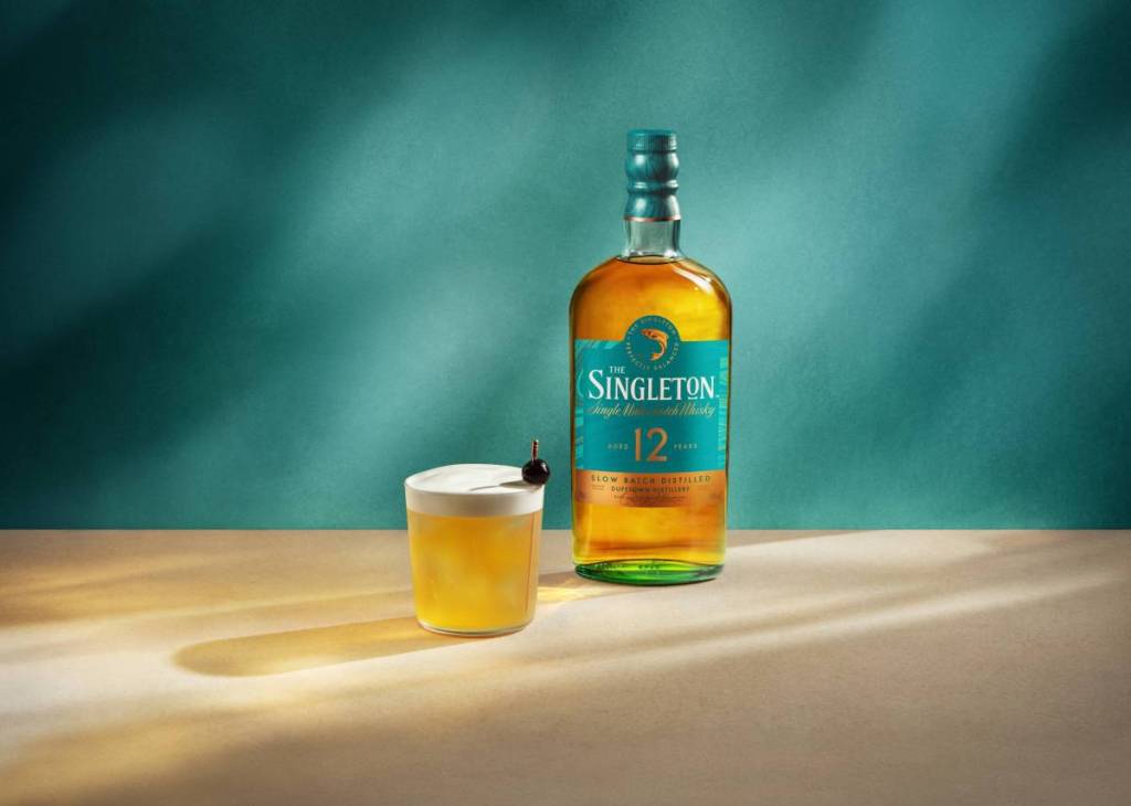 A bottle of Singleton whisky and a cocktail in front of a green background
