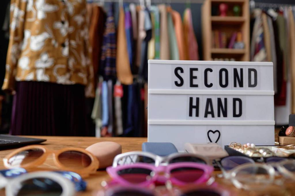 Bild von einem Schild mit der Beschriftung Second Hand in einem Geschäft mit Kleidung und vielen Sonnenbrillen