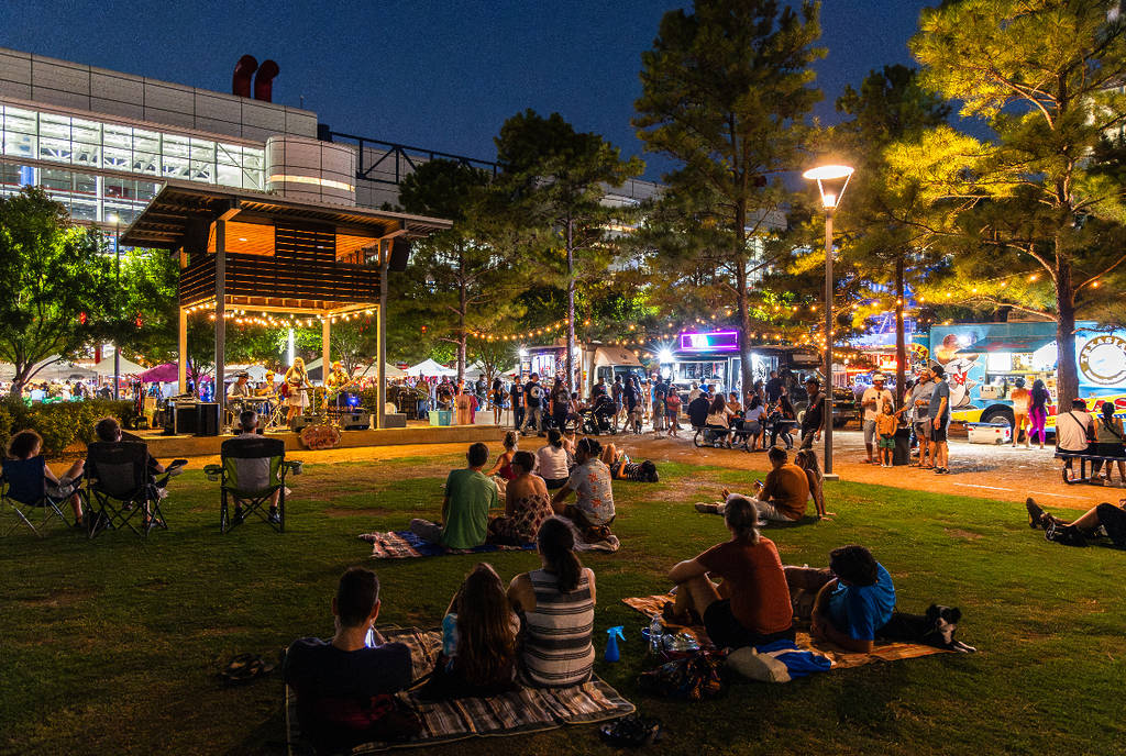 Image shows people sitting on a lawn in Houston for a night market.