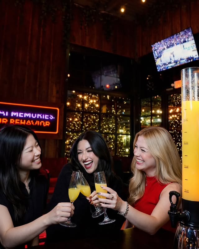 La imagen muestra a un par de mujeres brindando dentro de un bar deportivo. 