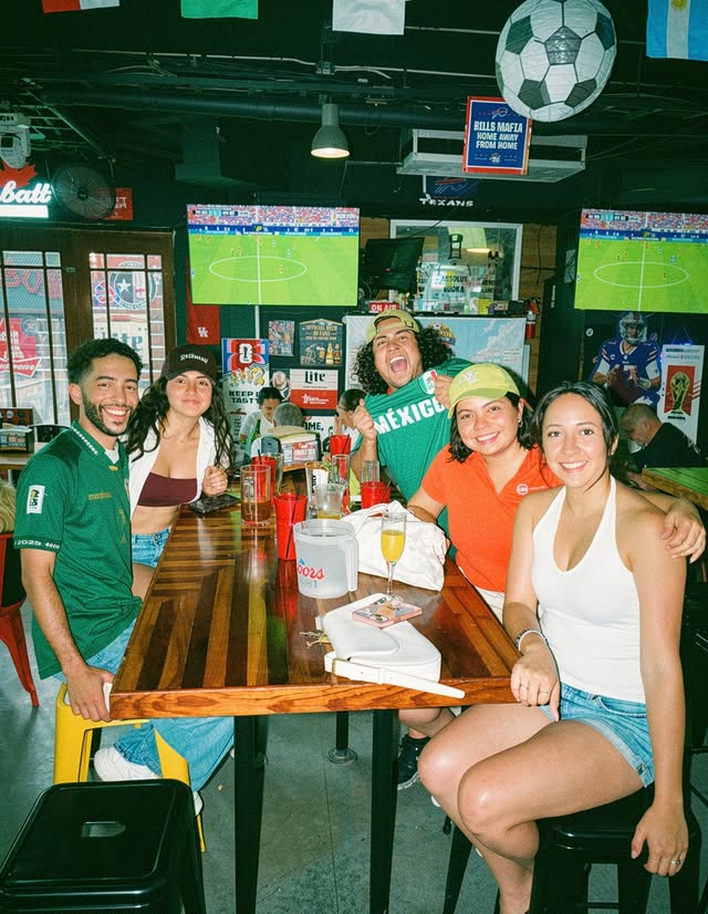 La imagen muestra una mesa de gente posando para una foto en Christian’s Tailgate, en Houston, durante una fiesta para ver un partido de fútbol. 