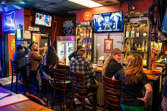 La imagen muestra a gente en la barra del Jake's Sports Bar. 