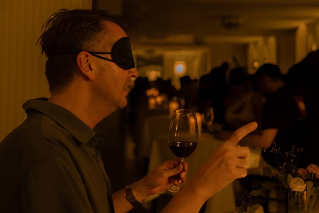 A blindfolded man pointing his finger at a Dining in the Dark experience