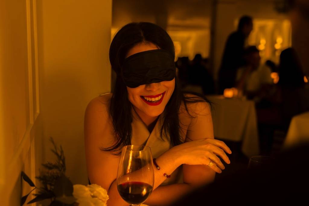 A blindfolded woman laughing at her table at a Dining in the Dark experience