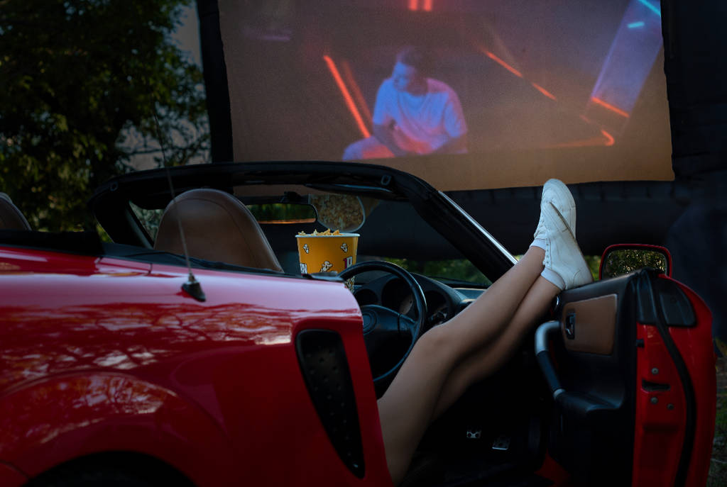 Imagen de una mujer en un coche descapotable viendo una película en un autocine.