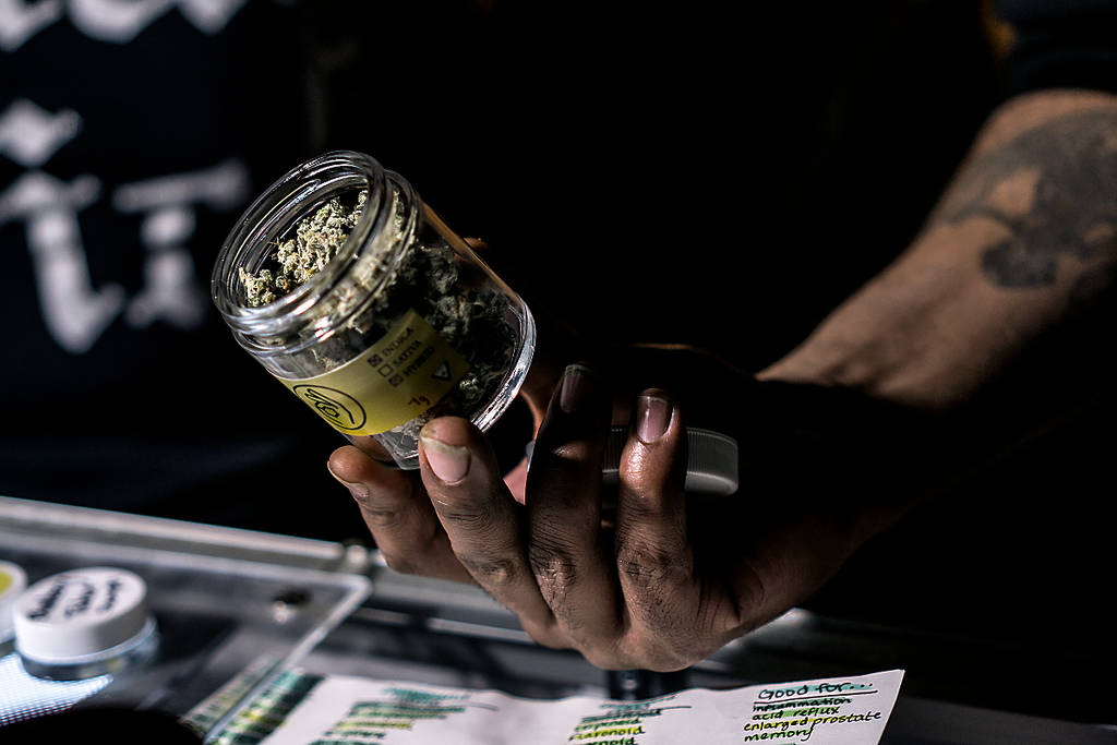 La imagen muestra a un cannabicultor sosteniendo un bote de marihuana en un dispensario.