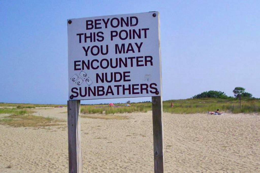 La imagen muestra un cartel en una playa nudista.