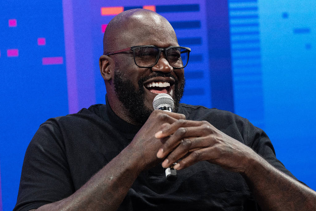 image shows Shaquille O'Neal laughing while holding a microphone.
