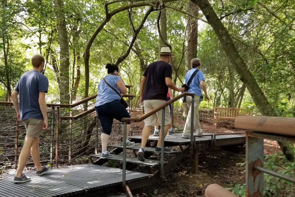 Image shows a group of people crossing a bridge along a trail inside the Houston Arboretum.