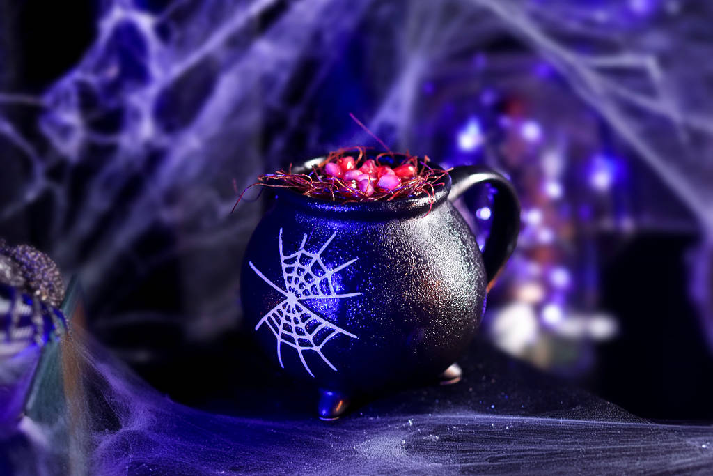 Image shows a cocktail at the Cursed Cauldron pop-up in Houston presented in a glass shaped like a coffin with a web print on it.