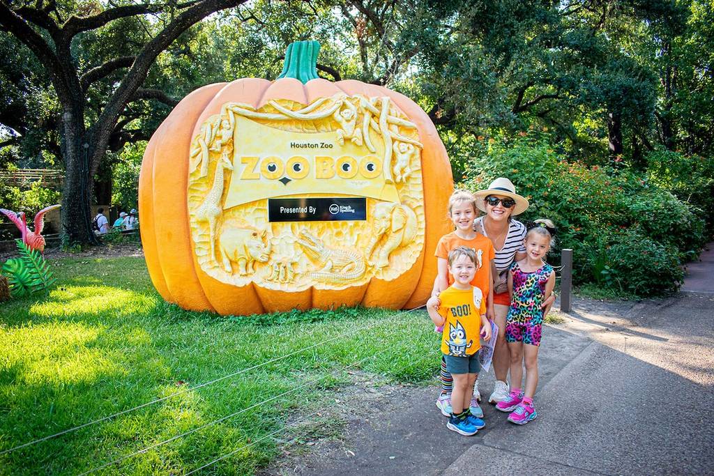Image shows a family posing in front of a giant pumpkin at the Houston Zoo.