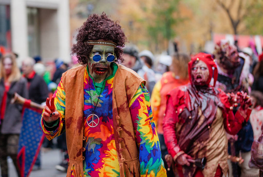 Imagen que muestra a personajes disfrazados en un desfile de Halloween en el que aparecen un personaje hippie zombi y un personaje diabólico.