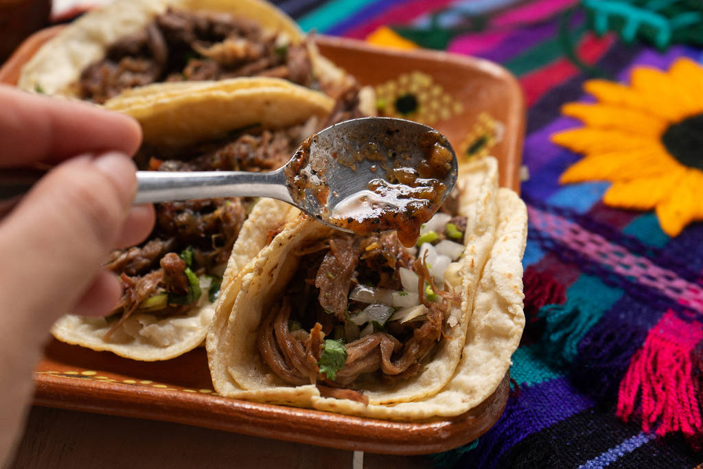 Image shows a tray of tacos on a plate with a spoon above them.