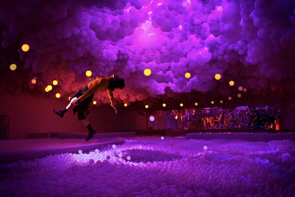 Image shows the HYPERCOSMO exhibit at the Houston Balloon Museum featuring a woman seemingly floating in the air in between two cloud installations.