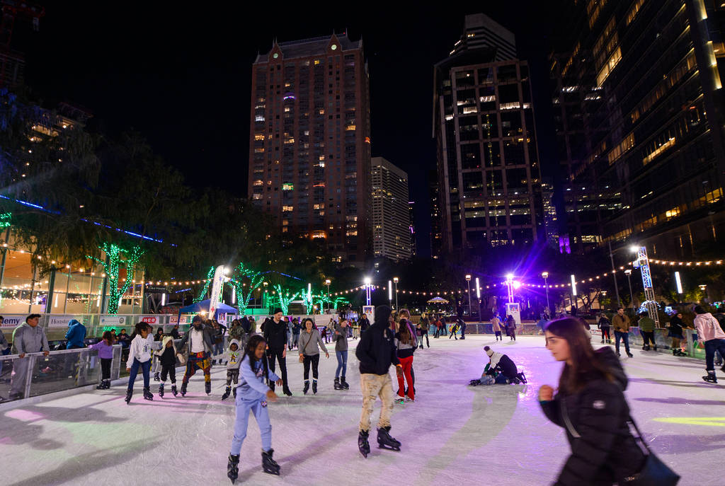 Image shows people skating at the Downtown Houston ice rink Ice at Discovery Green with the skyline in the background.