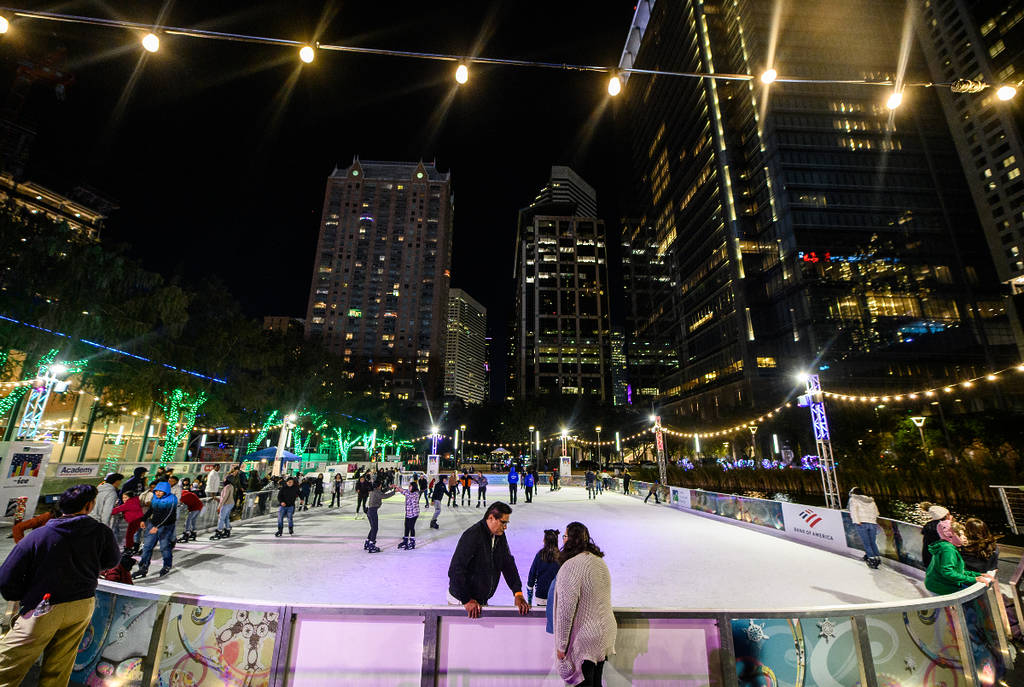 La imagen muestra a gente patinando en Ice at Discovery Green con el horizonte de Houston al fondo.