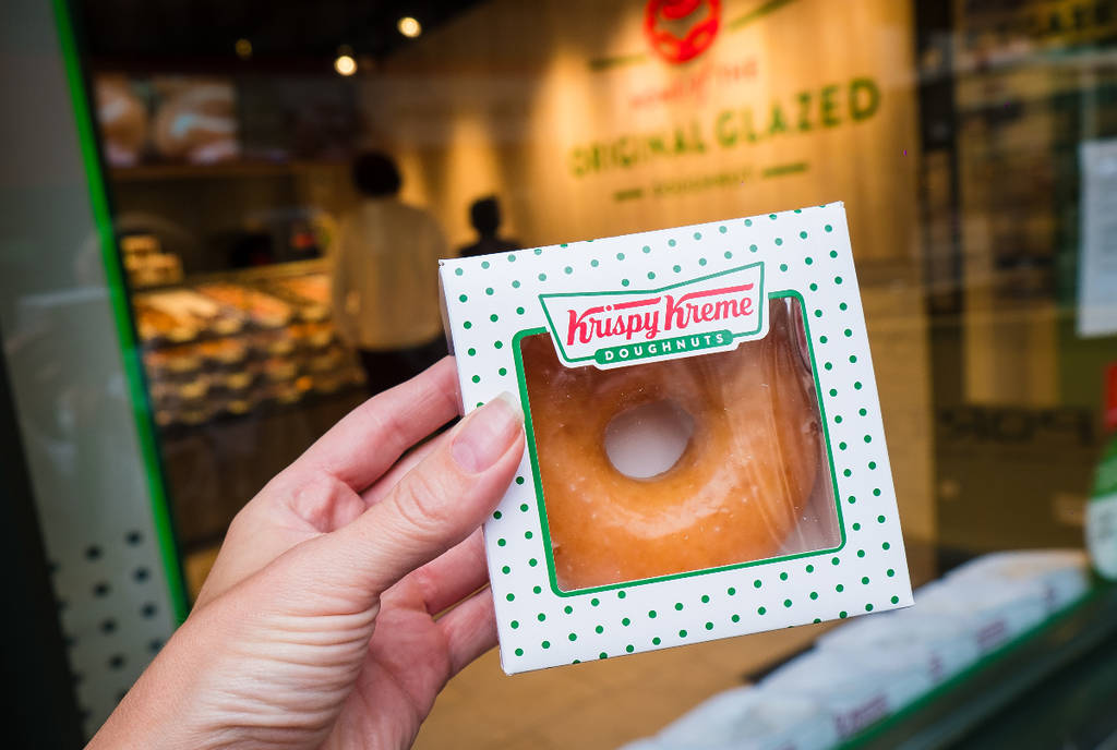 La imagen muestra a una persona sosteniendo un donut de Krispy Kreme empaquetado individualmente.