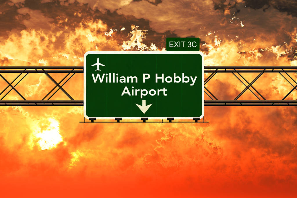 Image shows road signage for William P. Hobby Airport in Houston with a cloudy backdrop.