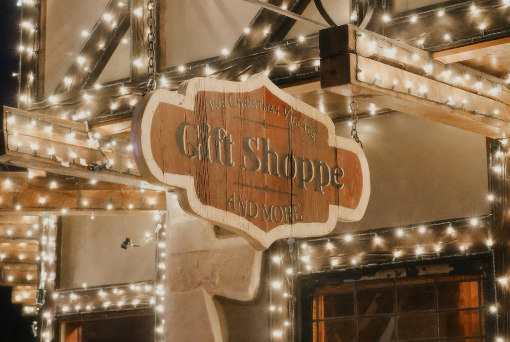 Image shows a gift shop signage adorned in Christmas lights at The Christmas Village in Huntsville, Texas.
