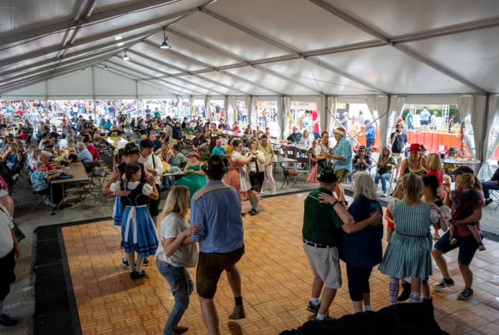Image shows a group of people dancing in German outfits inside a tent at the Tomball German Christmas Market outside Houston.