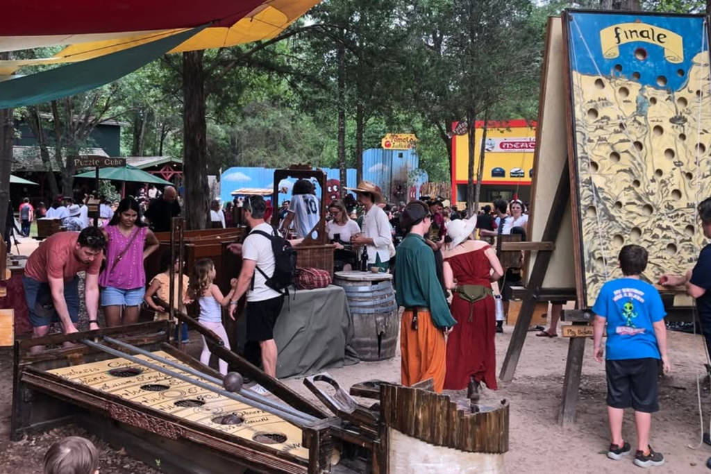 Image shows costumed attendants at a medieval festival with traditional games in the foreground.