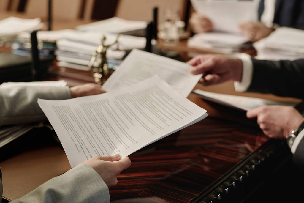 Image shows two people passing paperwork on a desk in an office.