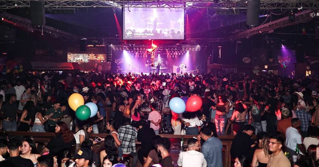 Image shows the interior of Cowboys Red River in Dallas during a live concert with attendees dancing in the foreground.