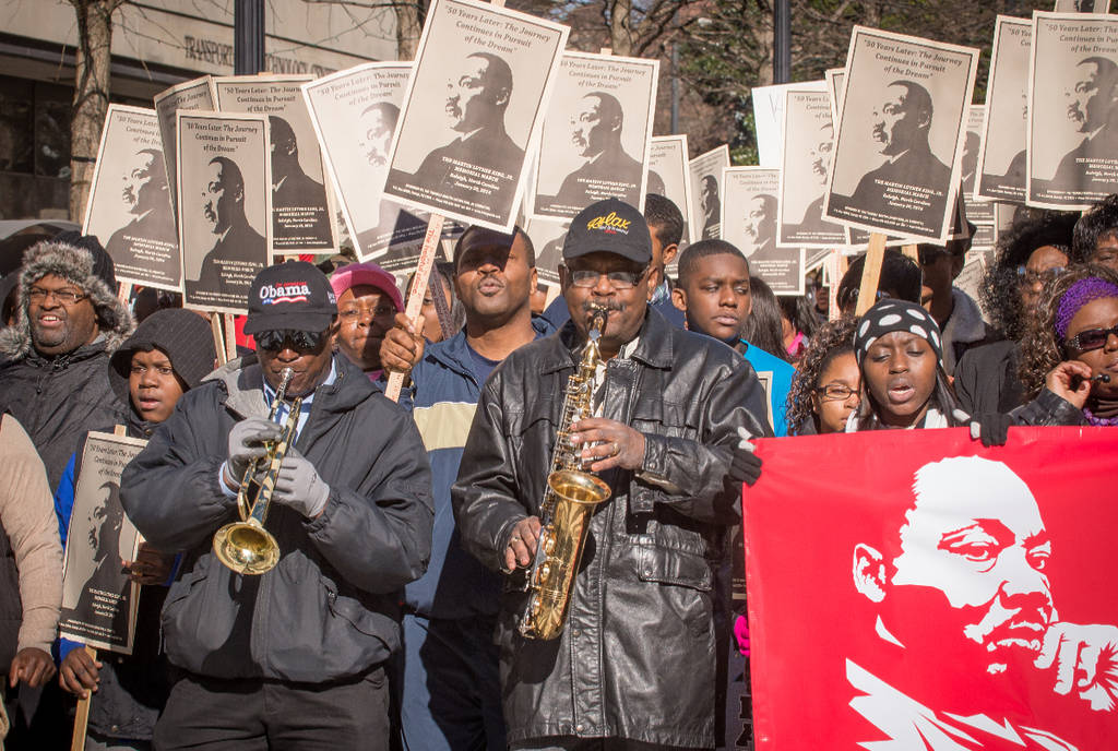 Image shows a group of people playing instruments and marching for a MLK Day Parade.