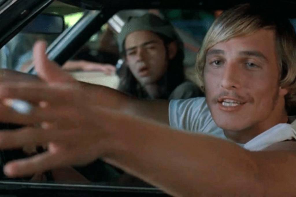 Image shows a still from the movie "Dazed & Confused" with Matthew McConaughey leaning out of the window.