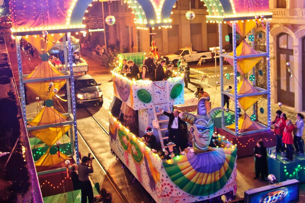 Image shows a glimpse of Mardi Gras! Galveston with a multicolored float leading a procession.