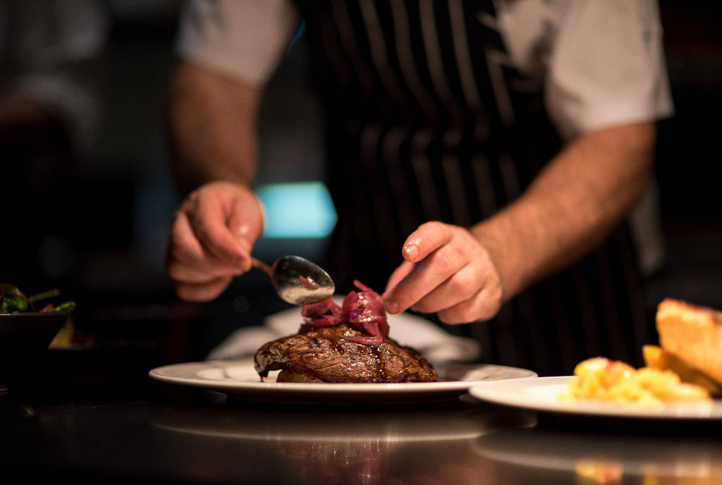 La imagen muestra a un chef emplatando un plato de carne.