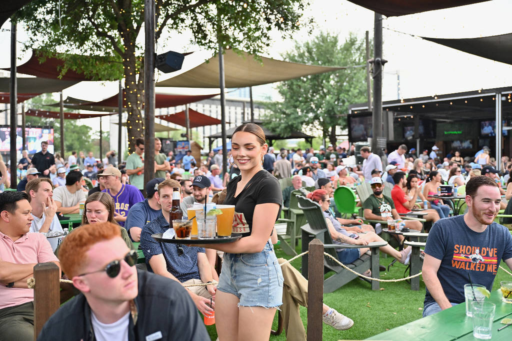 Image shows a server carrying a tray of drinks among a crowd of people hanging out on the patio at Kirby Ice House.