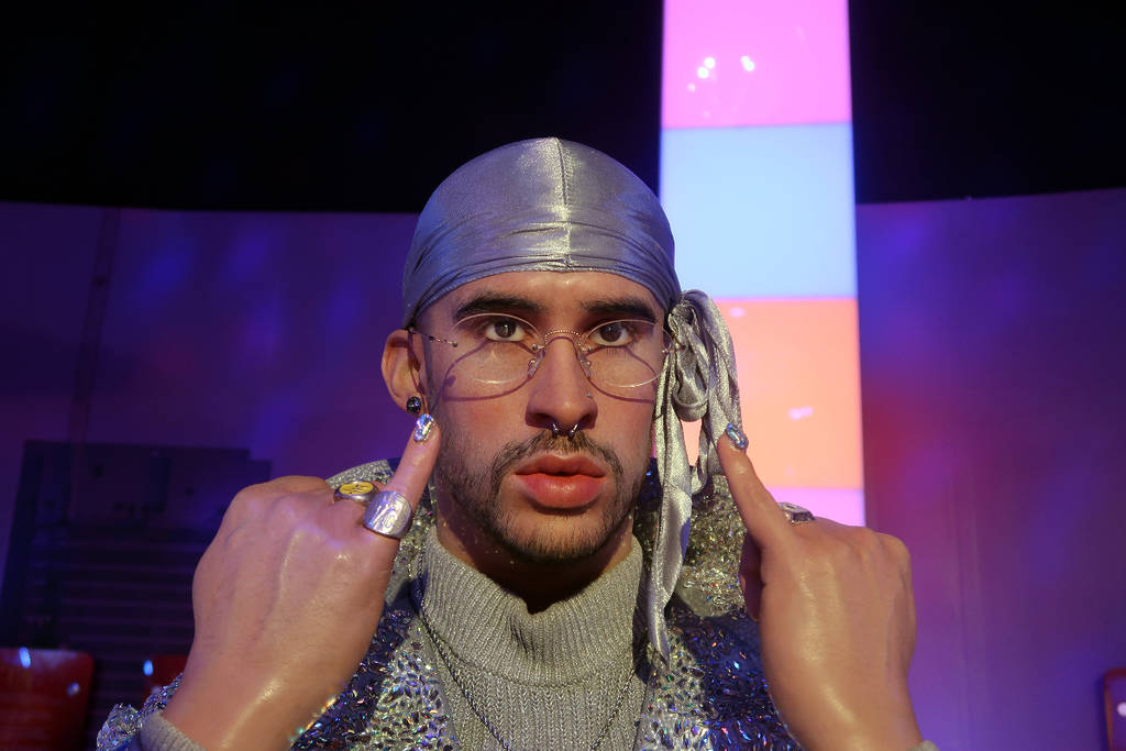Image shows a close up shot of Bad Bunny who is wearing a sparkly du-rag of sorts and holding his pinky fingers in the air.
