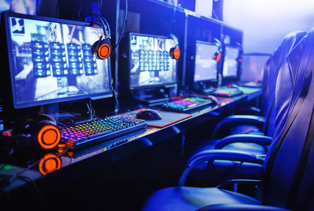 Image shows a row of computers and gaming chairs at a gaming cafe.